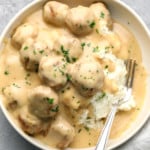 vegan Swedish meatballs covered in a creamy gravy and served on top of mashed potatoes in a white bowl with a fork.