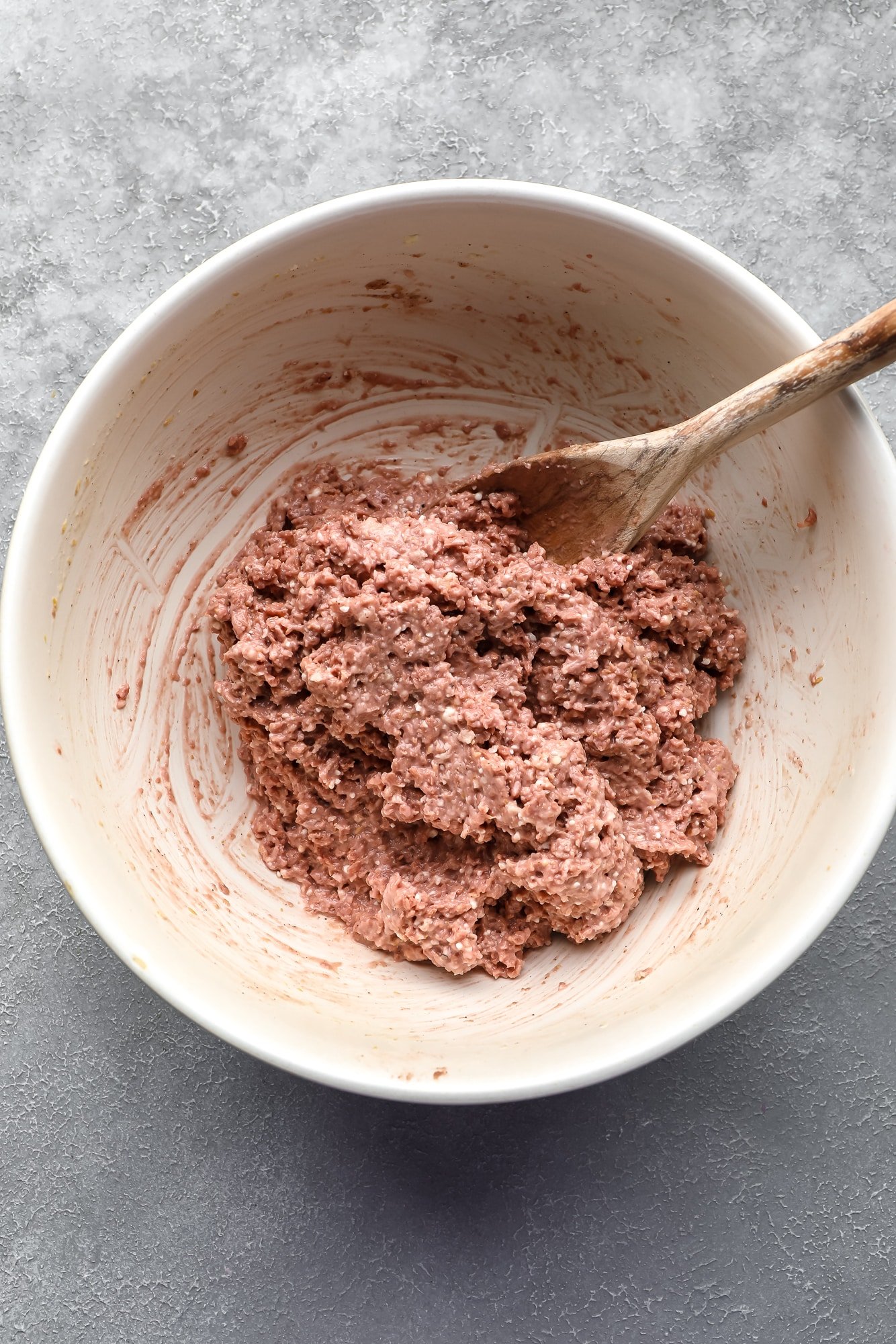 a vegan meatball mixture being stirred with a wooden spoon in a large white bowl.