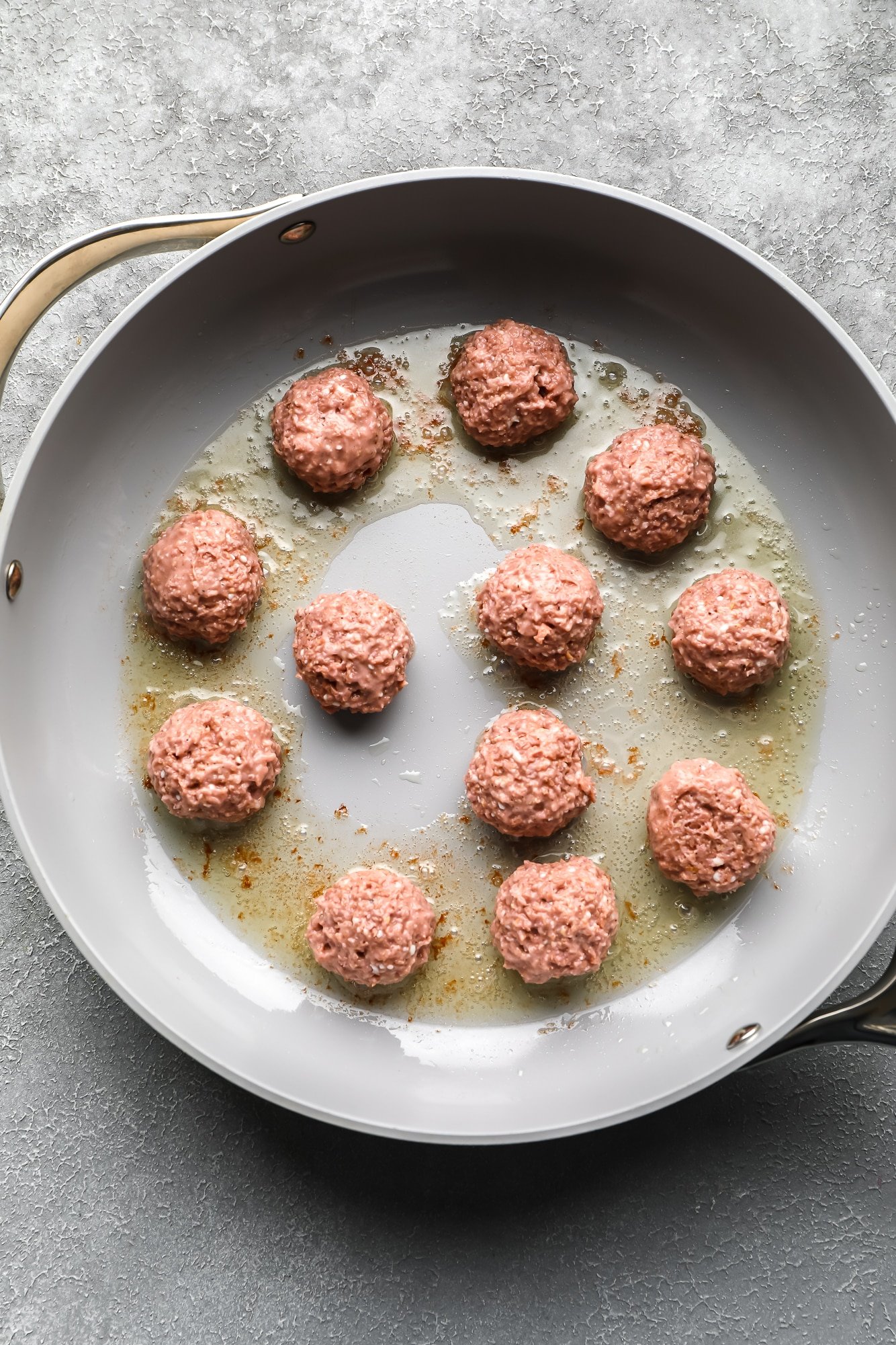 frying vegan meatballs in a large grey skillet.