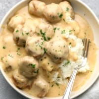 vegan Swedish meatballs covered in a creamy gravy and served on top of mashed potatoes in a white bowl with a fork.