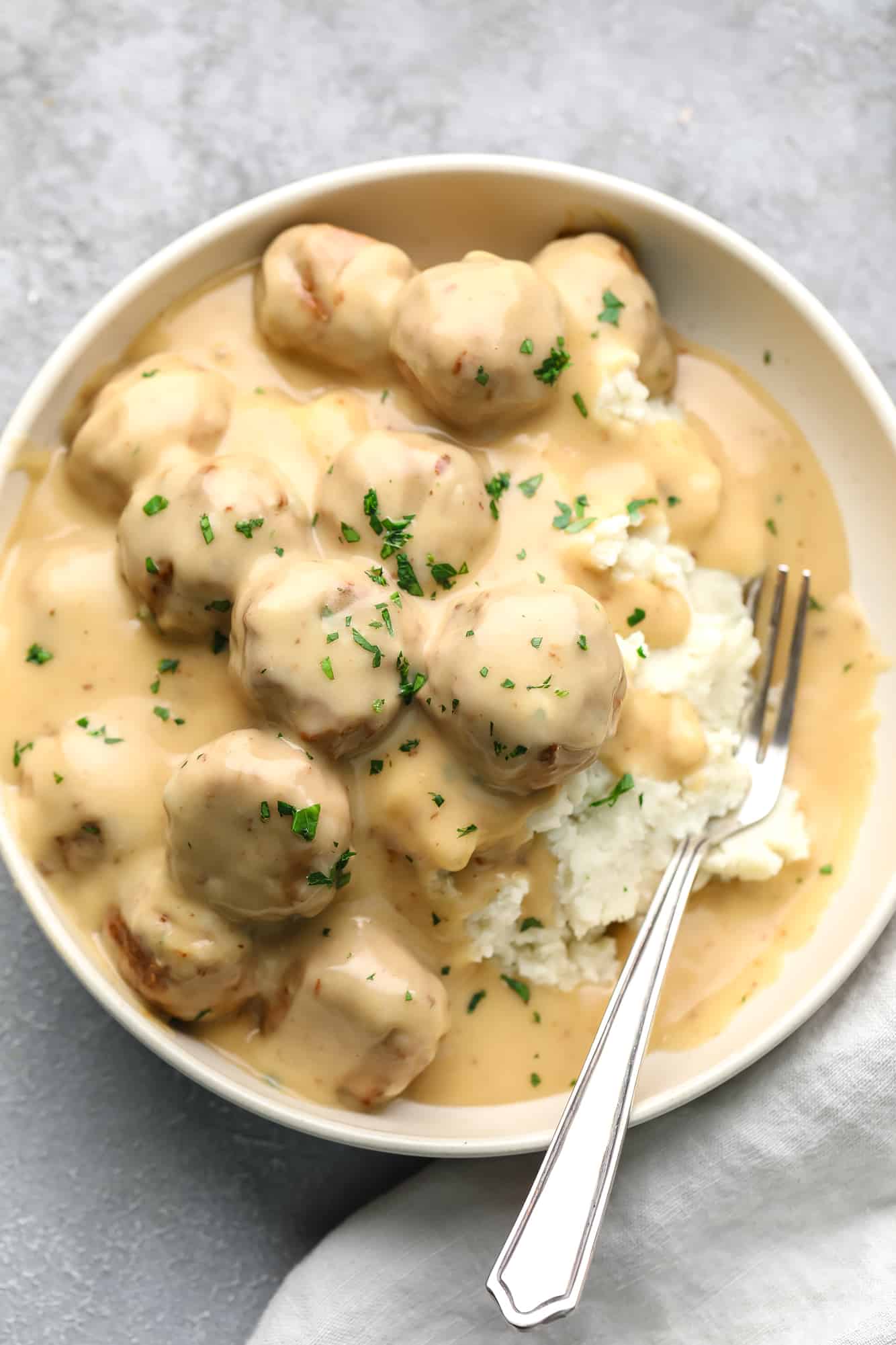 vegan Swedish meatballs covered in a creamy gravy and served on top of mashed potatoes in a white bowl with a fork.