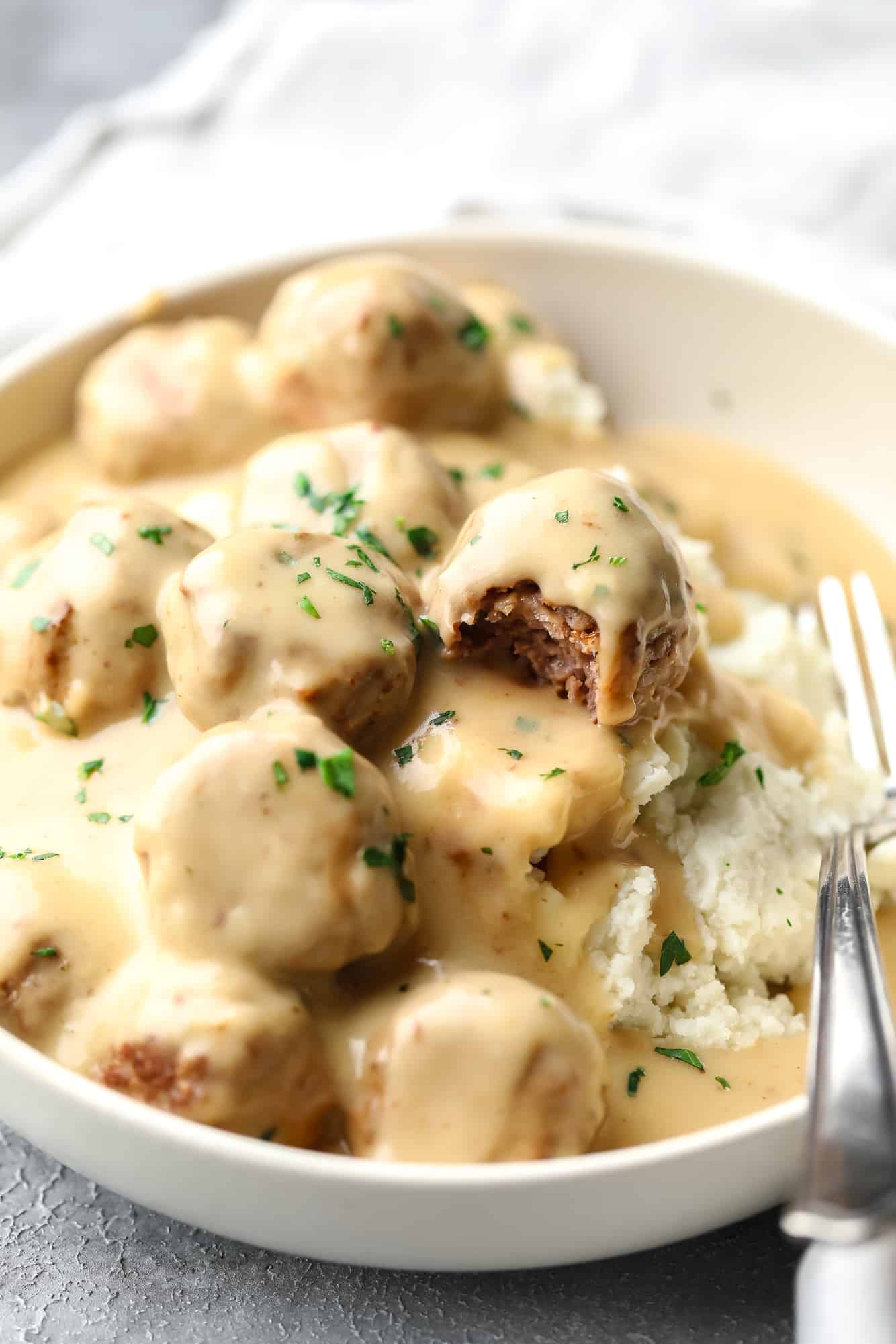 vegan Swedish meatballs covered in a creamy gravy and served on top of mashed potatoes in a white bowl with a fork.