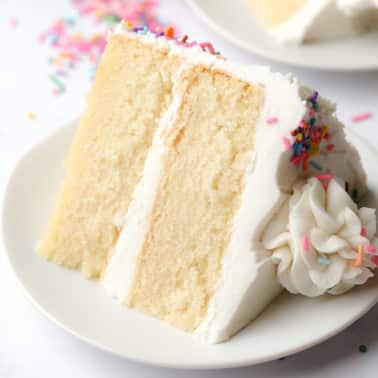 square image of a piece of vanilla cake on a white plate with some colorful sprinkles