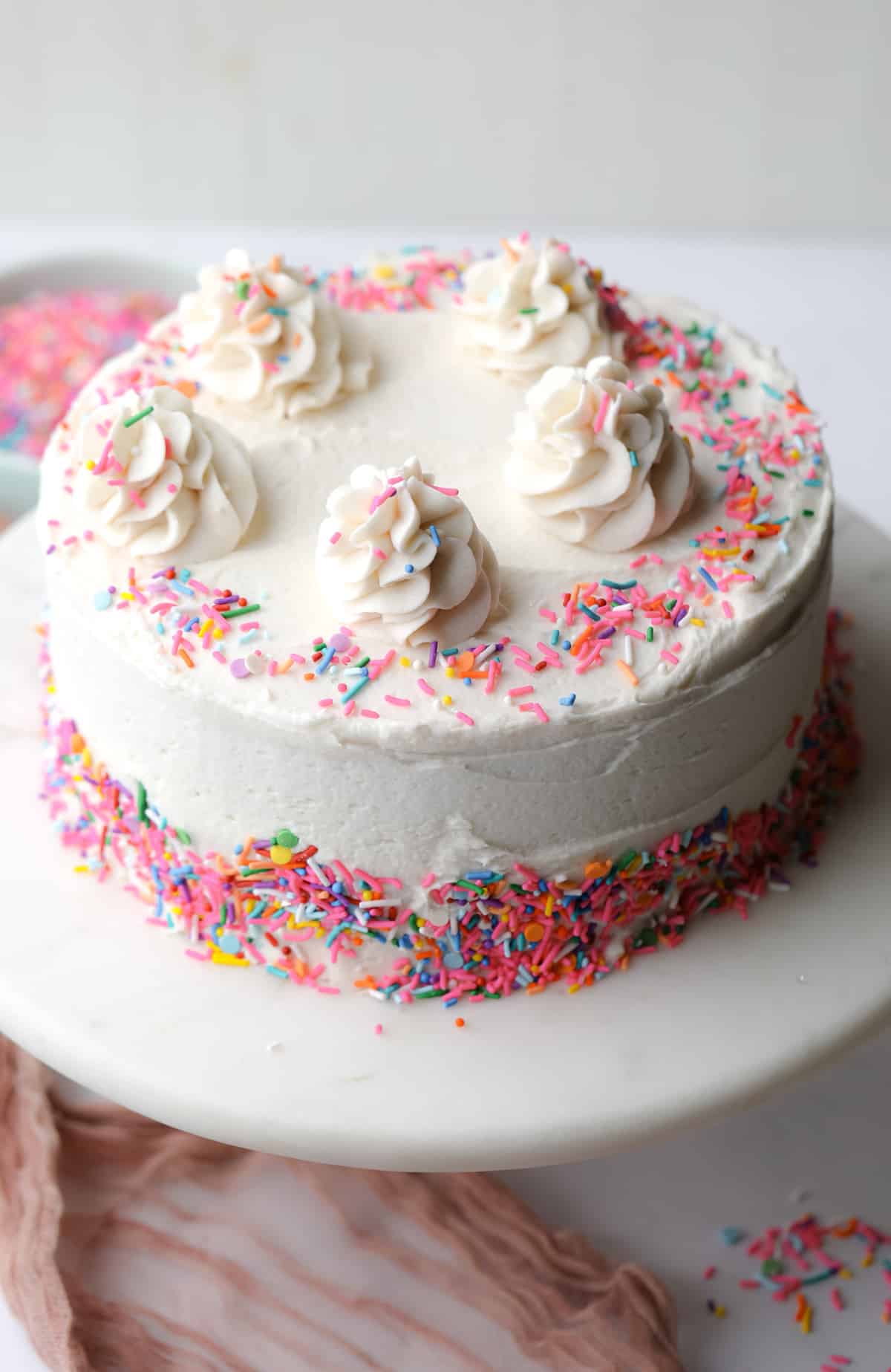 decorated, frosted cake with white frosting and colorful sprinkles on white background