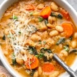 a white bowl full of white bean soup topped with shredded vegan parmesan.