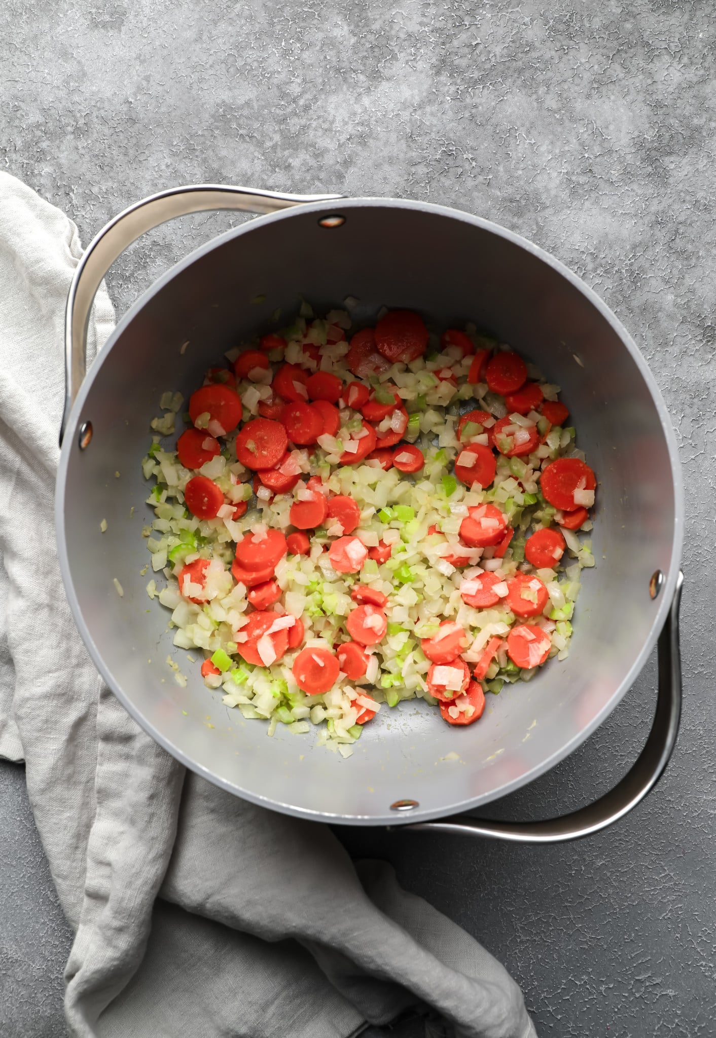 cooking carrots, onions, and celery in a large grey pot.