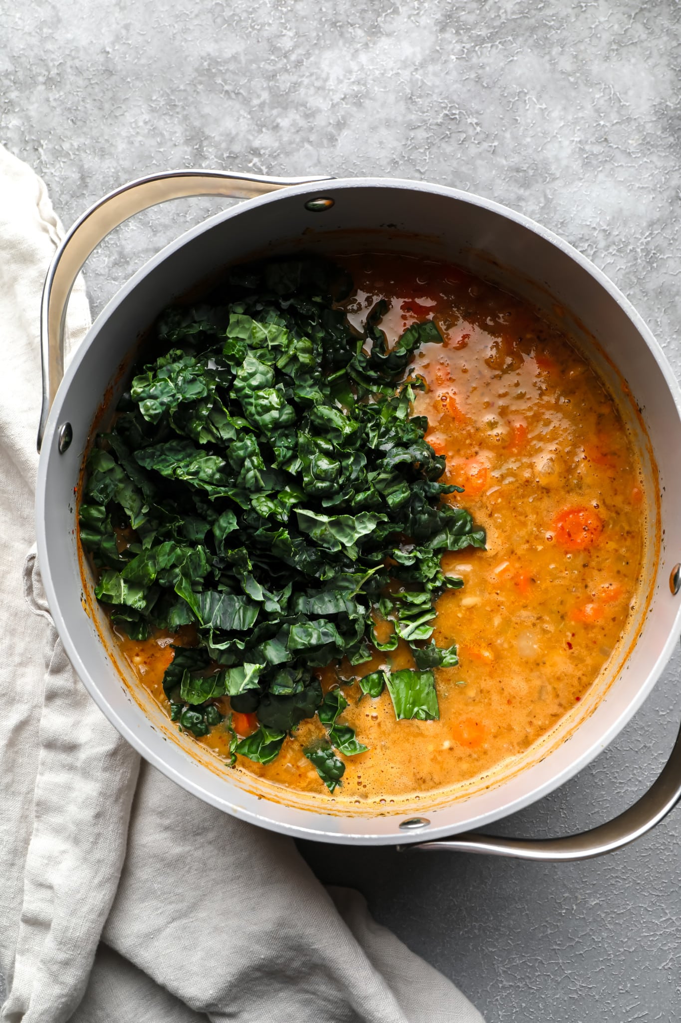 chopped kale on top of a batch of white bean soup in a large grey pot.