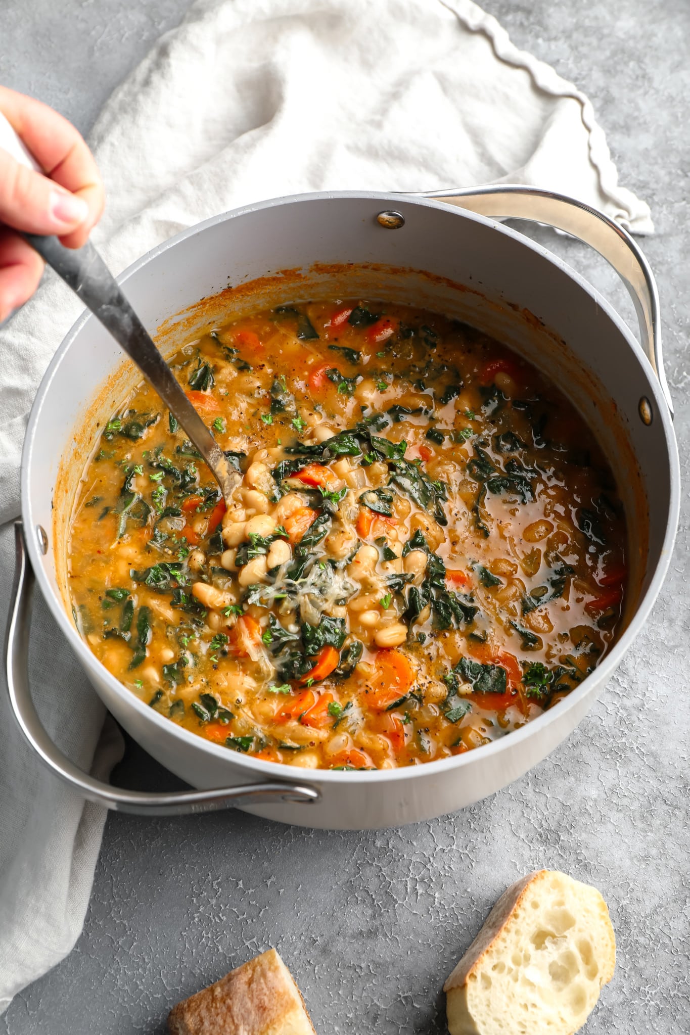 womans hand using a spoon to stir white bean soup in a large pot.