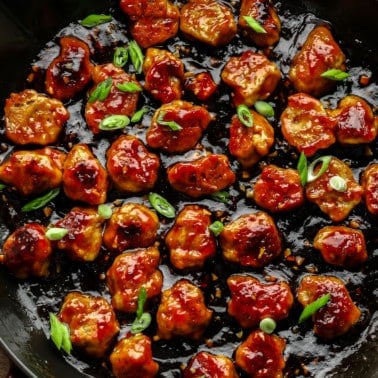 close up on bite-sized seitan nuggets covered in a "honey" ginger sauce and cooking in a large black skillet.