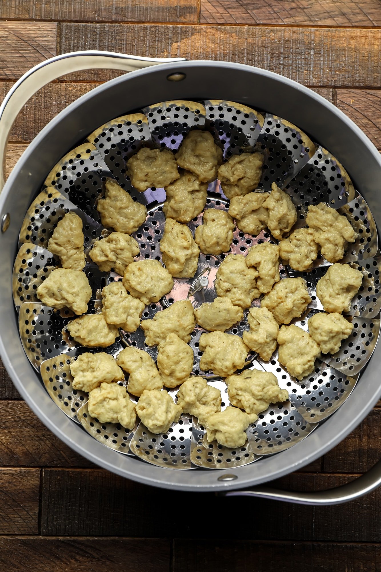 raw seitan nuggets on a steamer basket in a large grey pot.