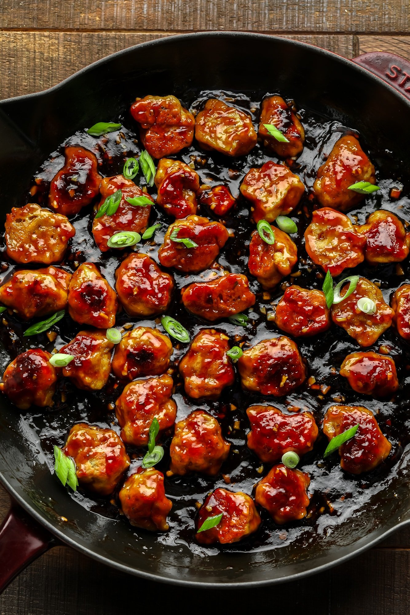 close up on bite-sized seitan nuggets covered in a "honey" ginger sauce and cooking in a large black skillet.