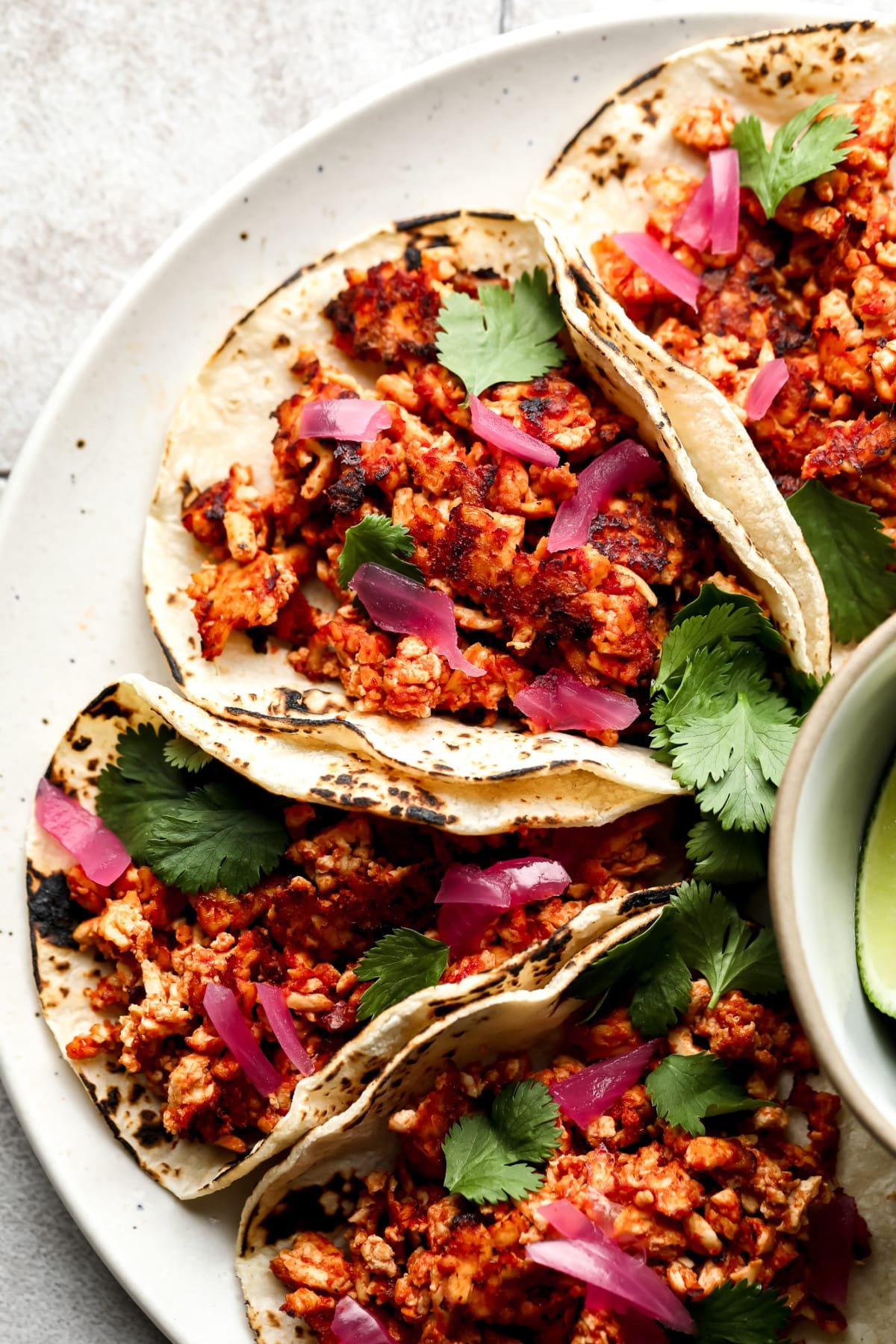 4 tofu tacos with corn tortillas, cilantro and pickled red onion on a plate