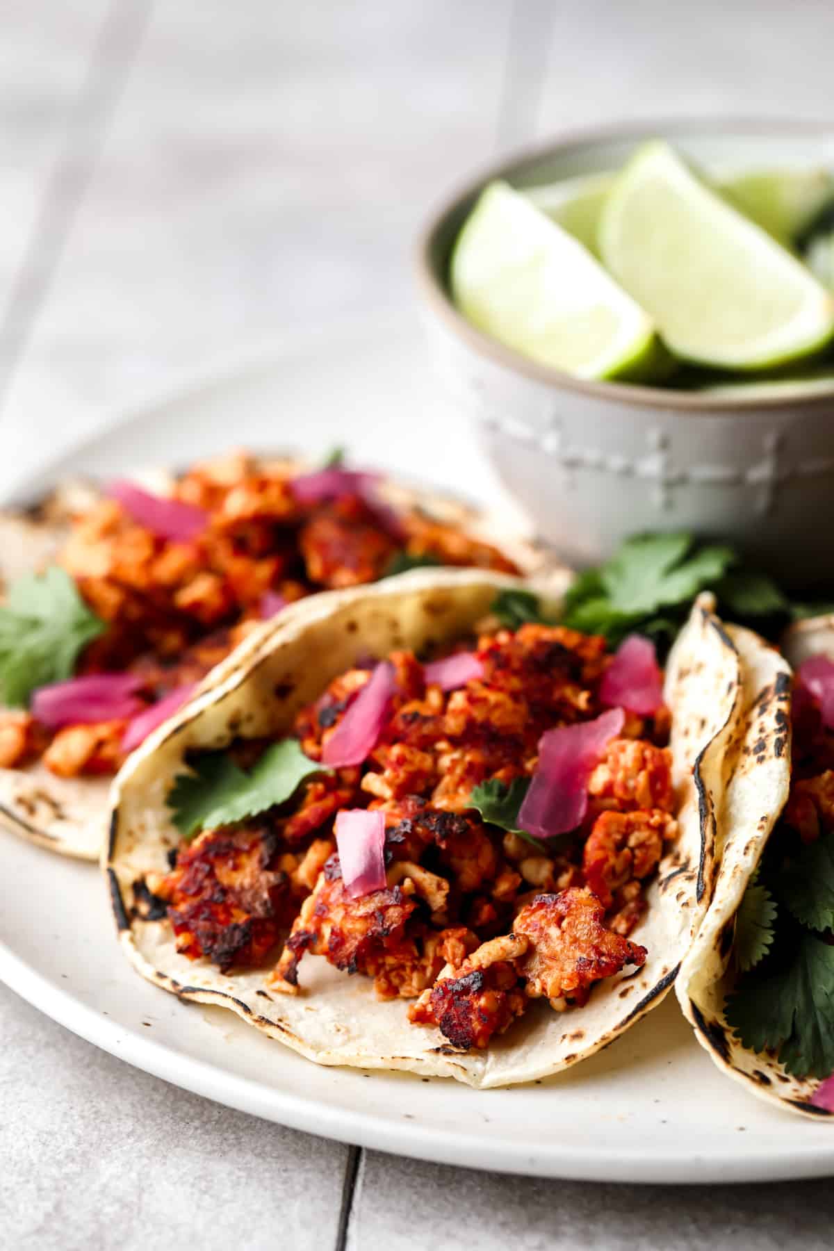 tacos with tofu filling on a plate with grey background and limes in a bowl