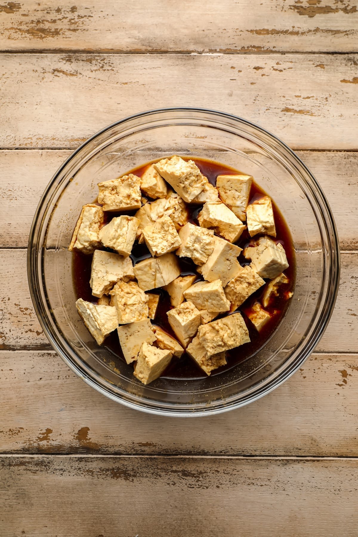 ripped tofu chunks in a glass bowl with soy sauce marinade on wooden background