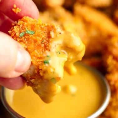 breaded nugget being dipped in yellow sauce with a bite taken out of it