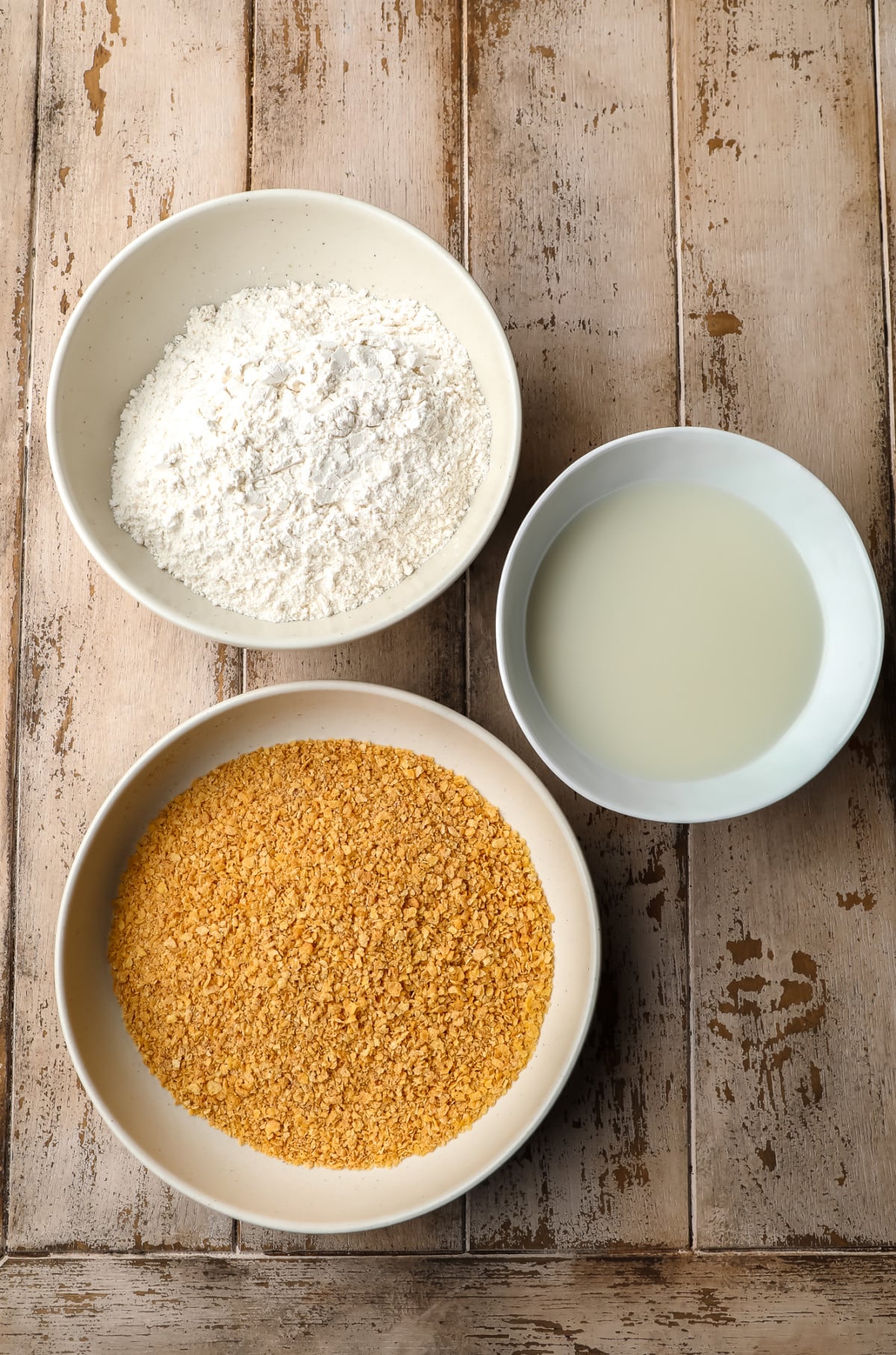 bowl with breadcrumbs, flour and milk on wooden background