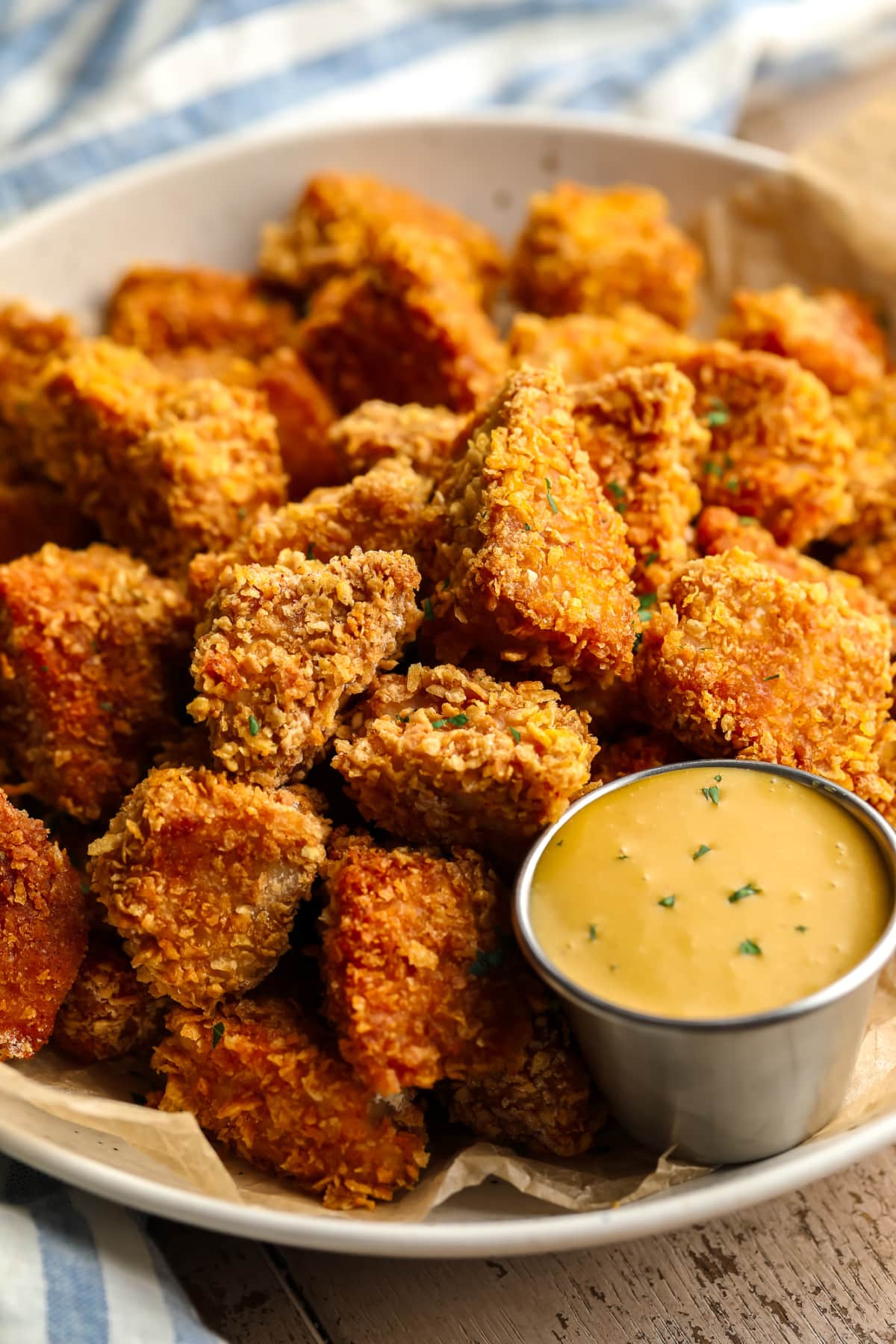 crispy breaded vegan chicken nuggets in a shallow bowl with yellow dipping sauce, blue towel in background