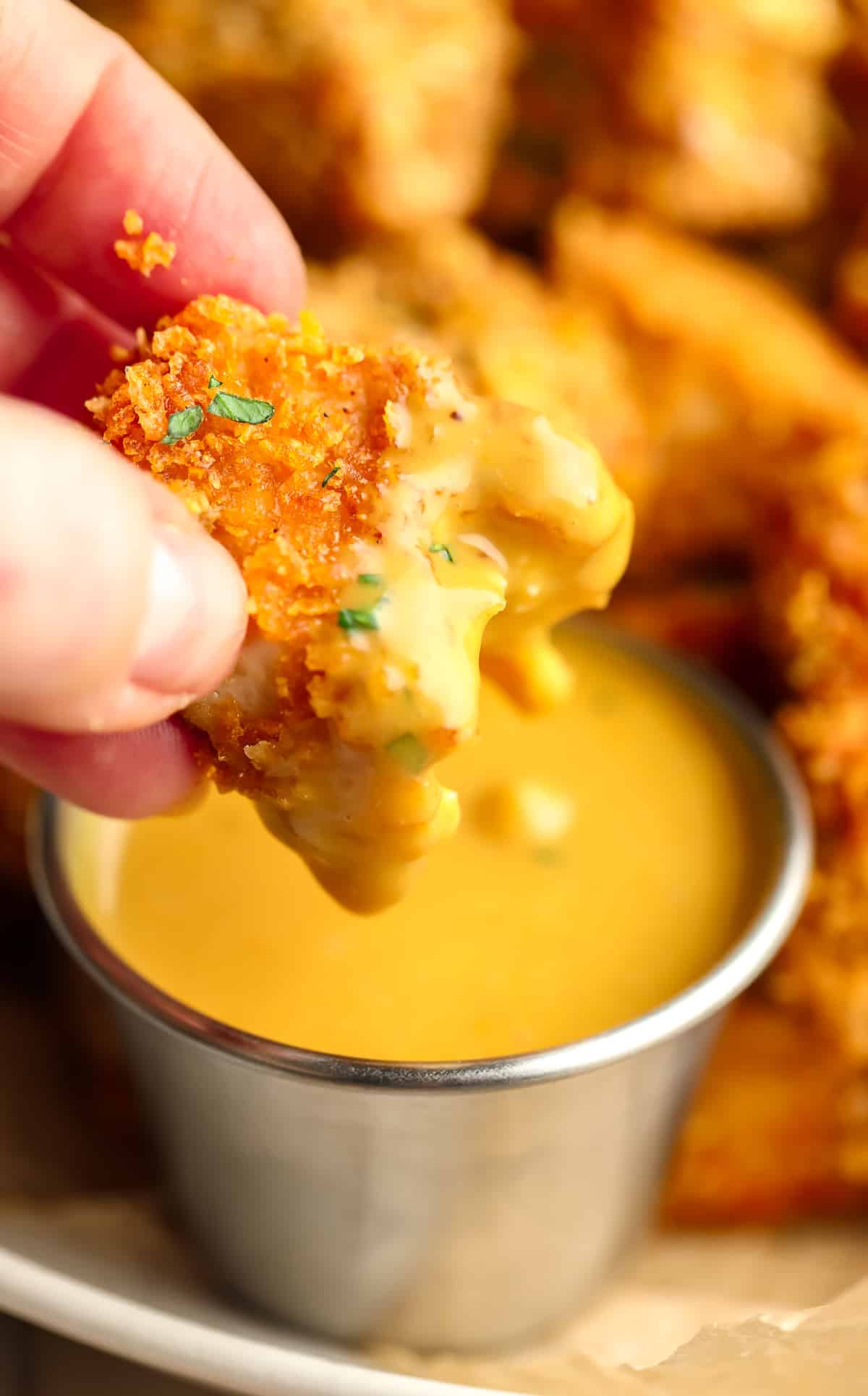 bite taken out of a vegan chicken nugget, being dipped by a hand in yellow sauce