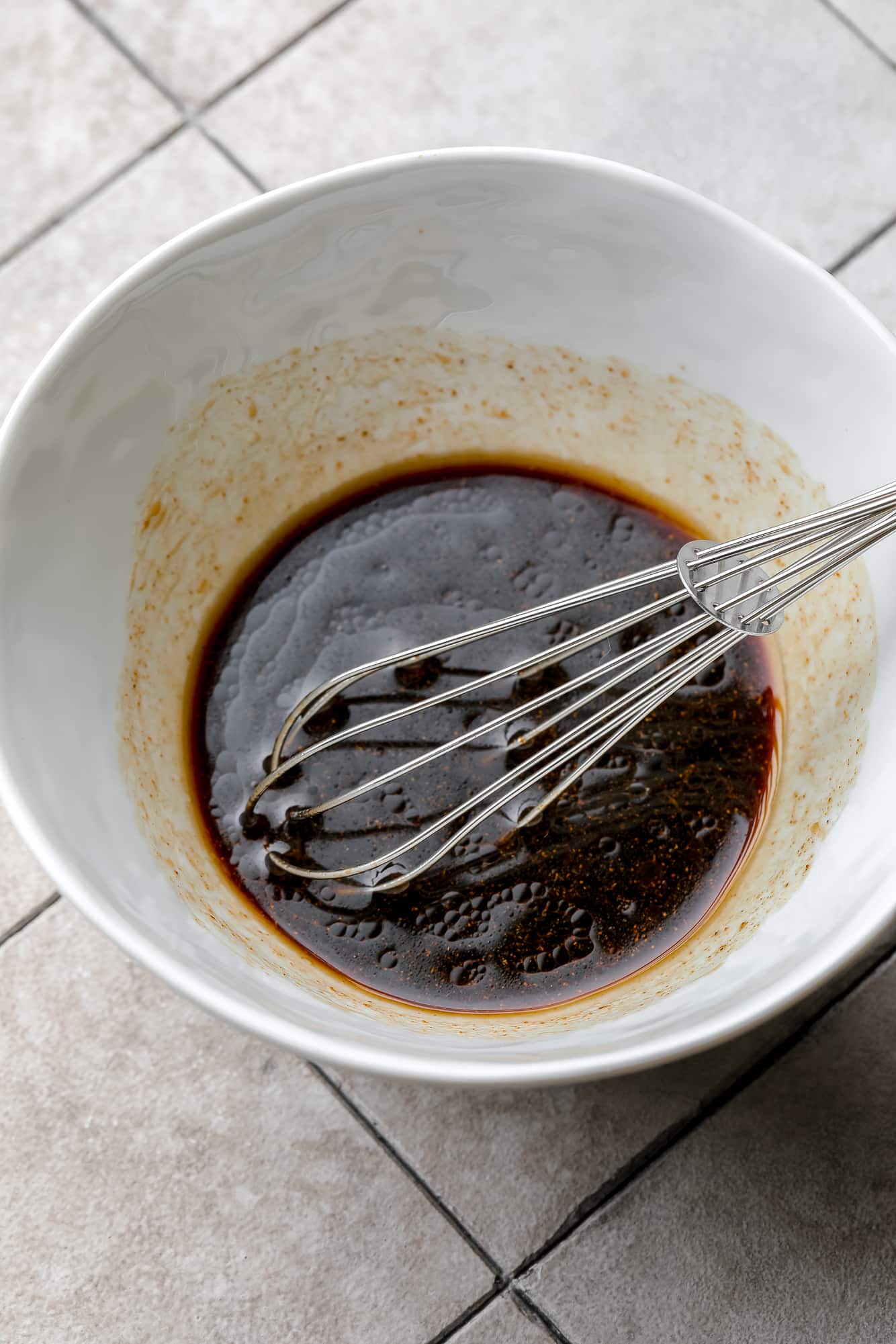 whisking vegan lo mein sauce in a white bowl.