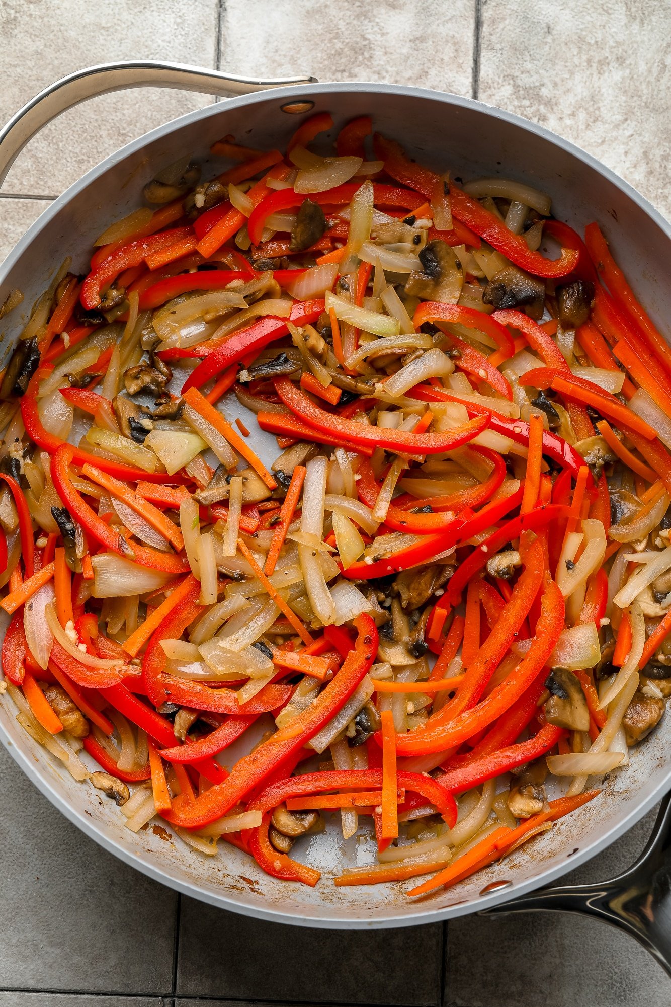 cooking thinly sliced vegetables in a large gray skillet.