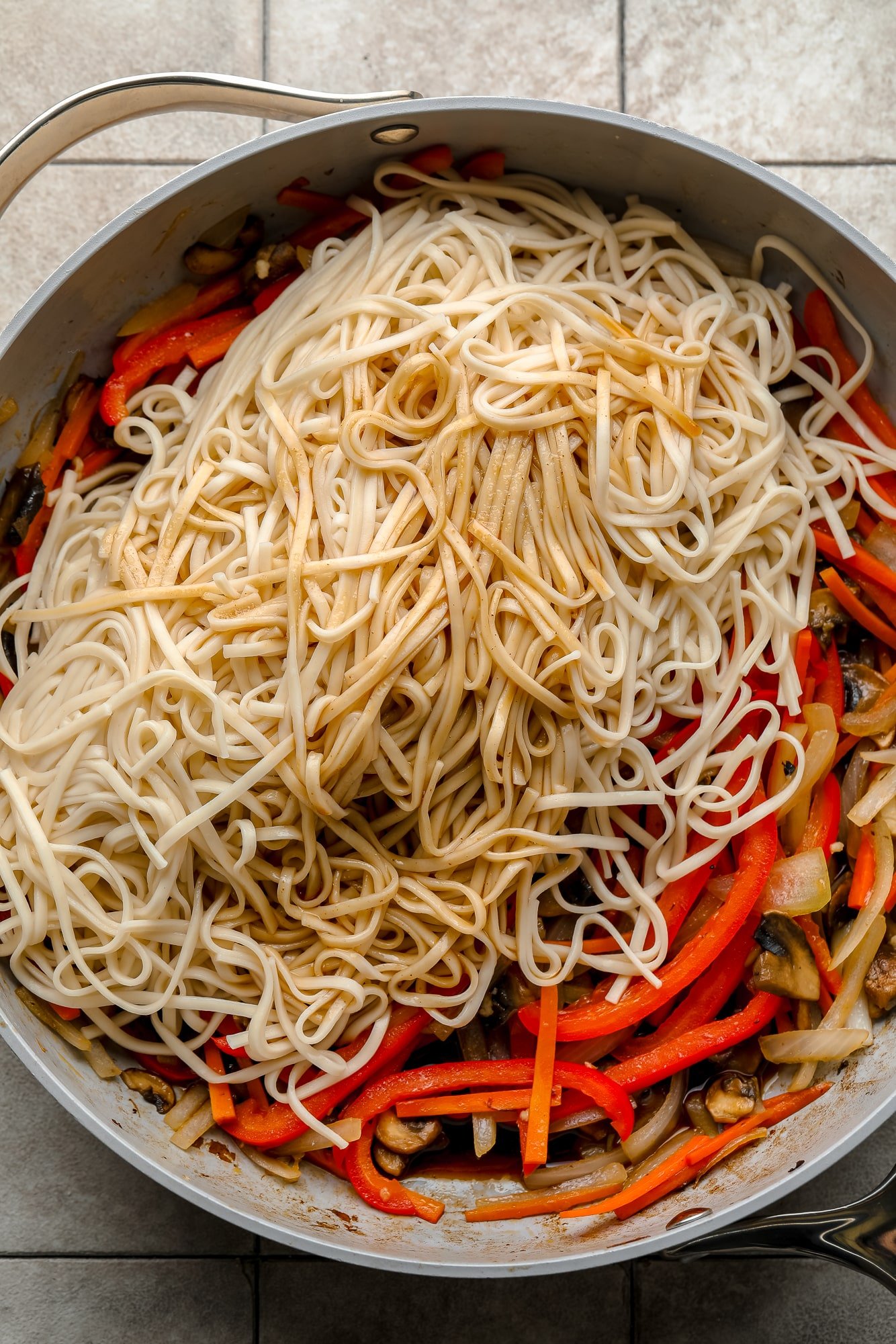 cooked noodles on top of stir-fried vegetables in a large gray skillet.