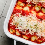 close up on vegan manicotti topped with vegan mozzarella in a white baking dish.