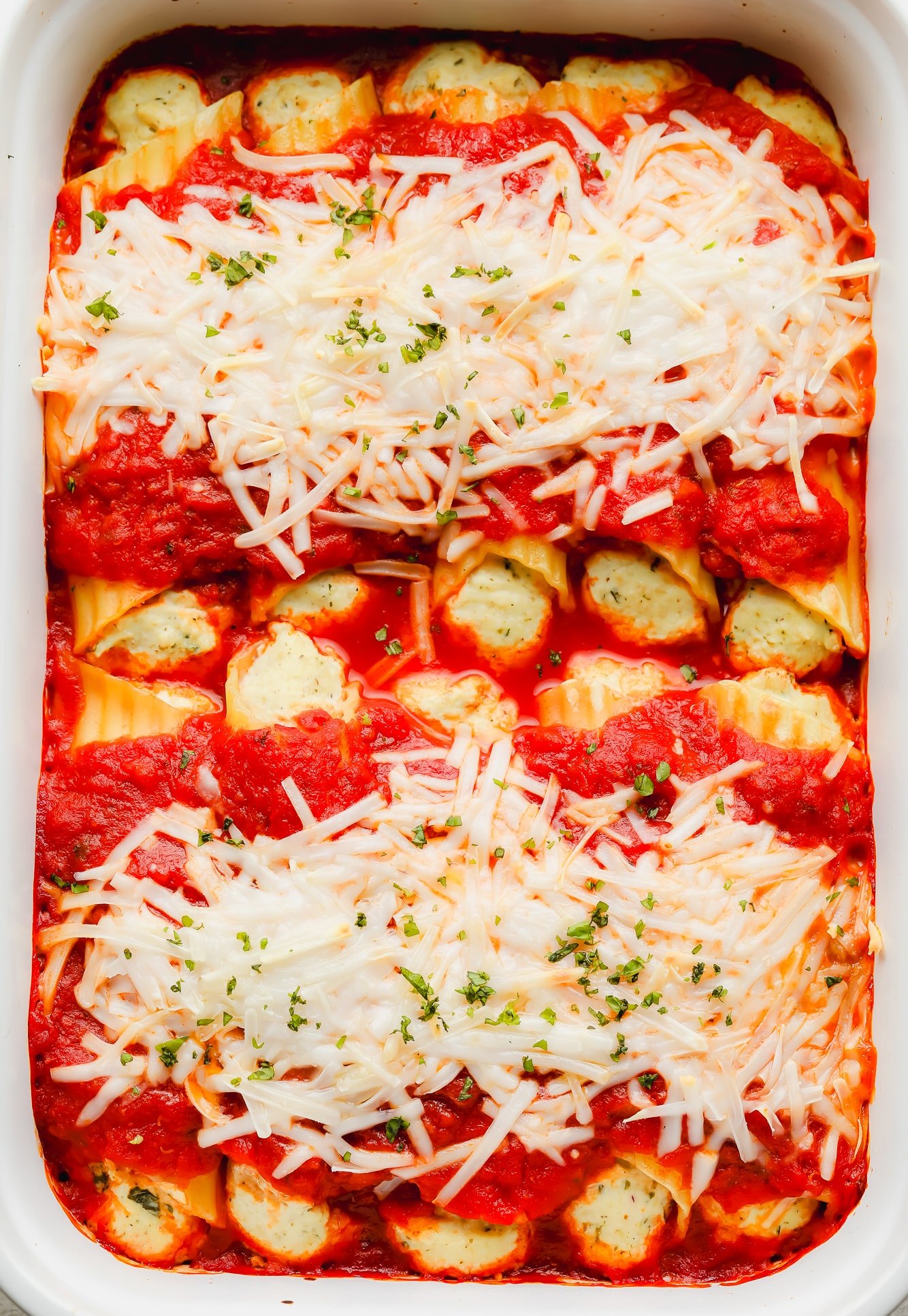 baked manicotti topped with marinara sauce and vegan mozzarella in a white baking dish.