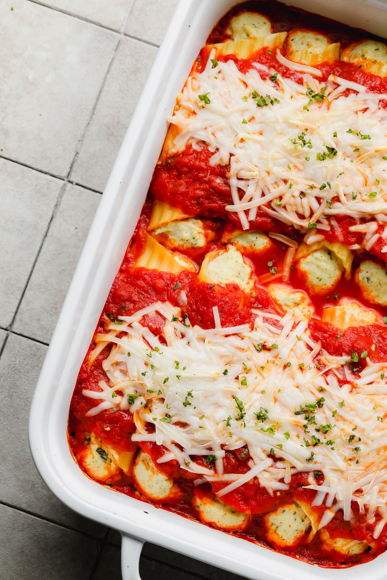 baked vegan manicotti topped with marinara sauce and vegan mozzarella in a white baking dish.