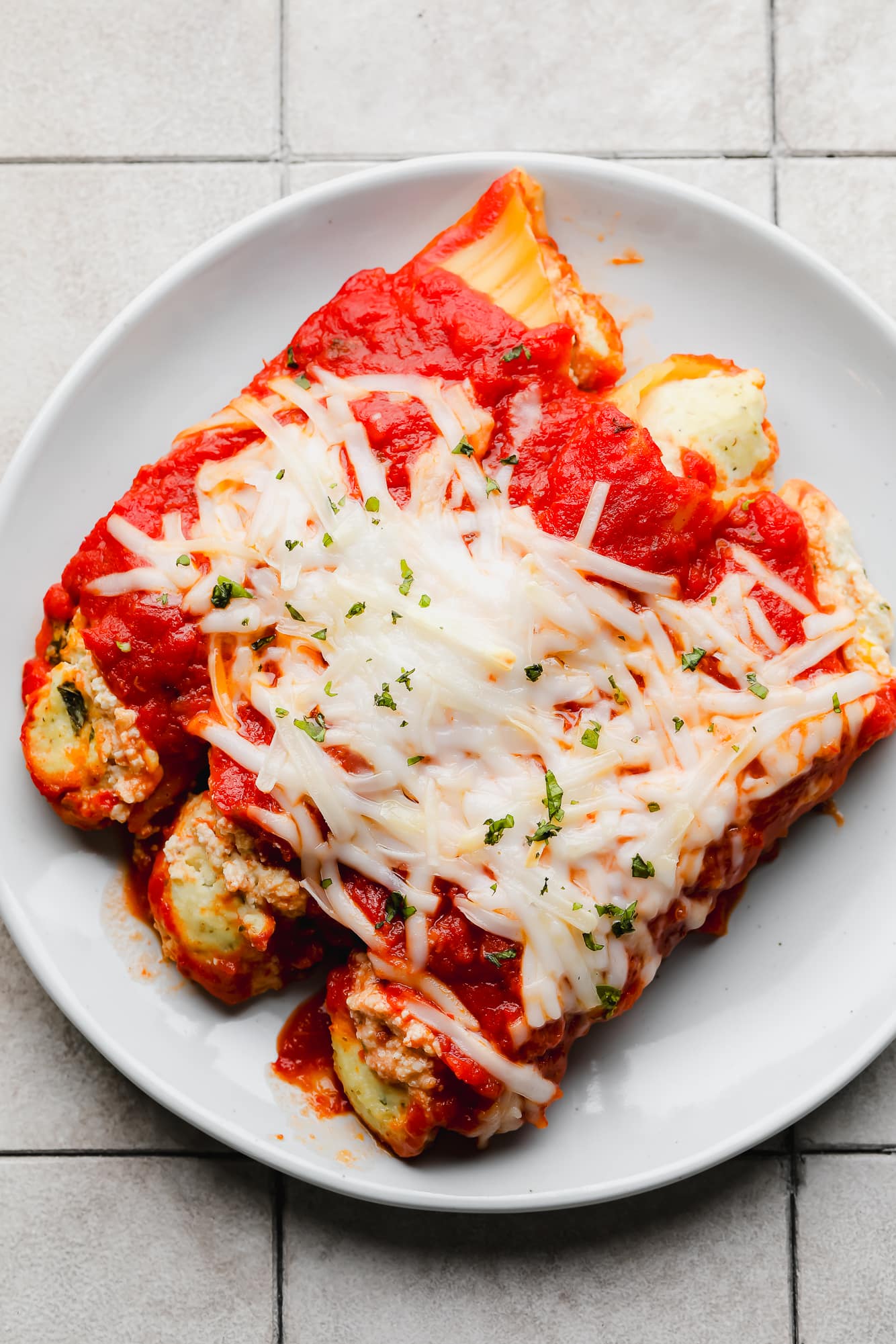 3 baked vegan manicotti shells topped with vegan mozzarella on a white plate.