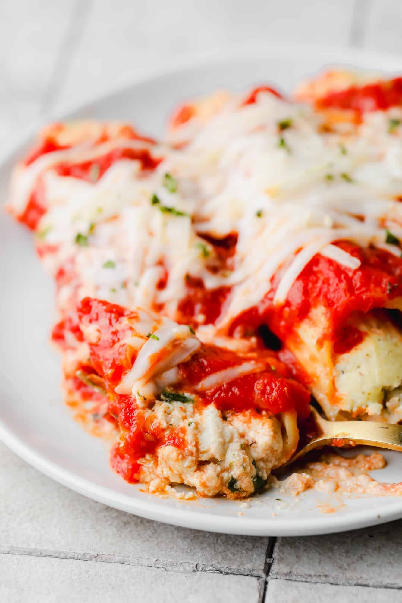 close up on a fork taking a scoop of vegan manicotti from a serving on a white plate.