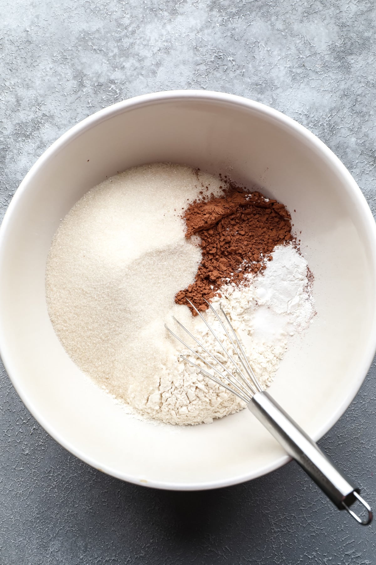 bowl with flour, sugar, cocoa and a whisk on grey background