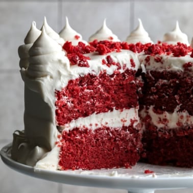 square image of a red cake with white frosting and red crumbles on top