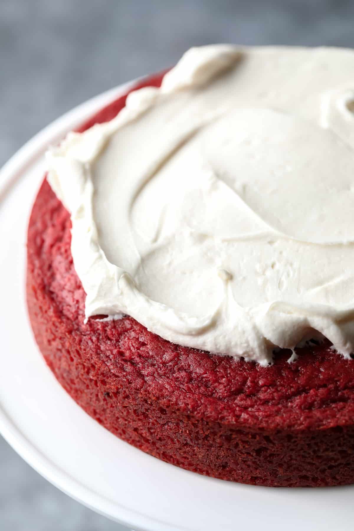 white frosting being spread on red cake