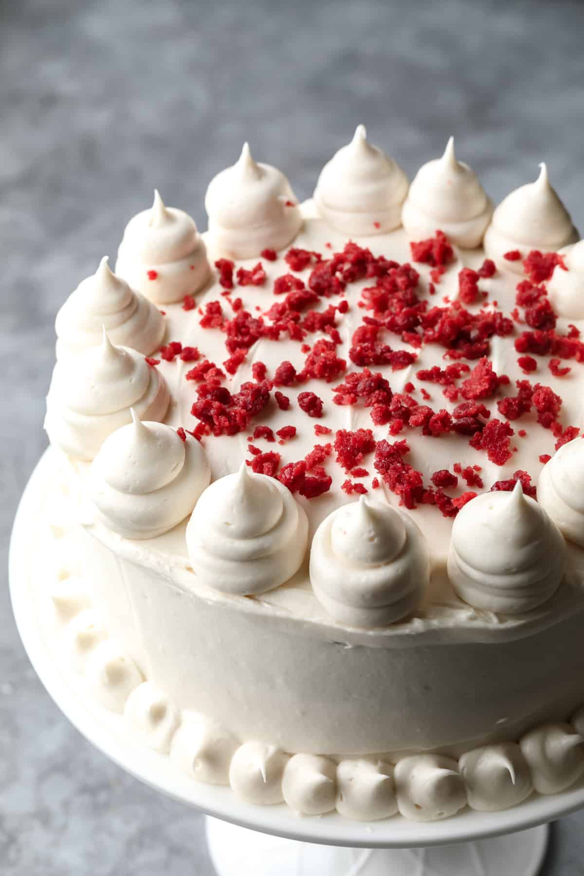 frosting vegan red velvet cake with red crumbles and piped cream cheese frosting all over