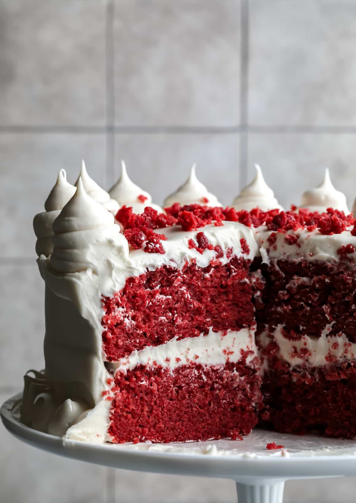 cut into cake on stand, red with white frosting, grey background