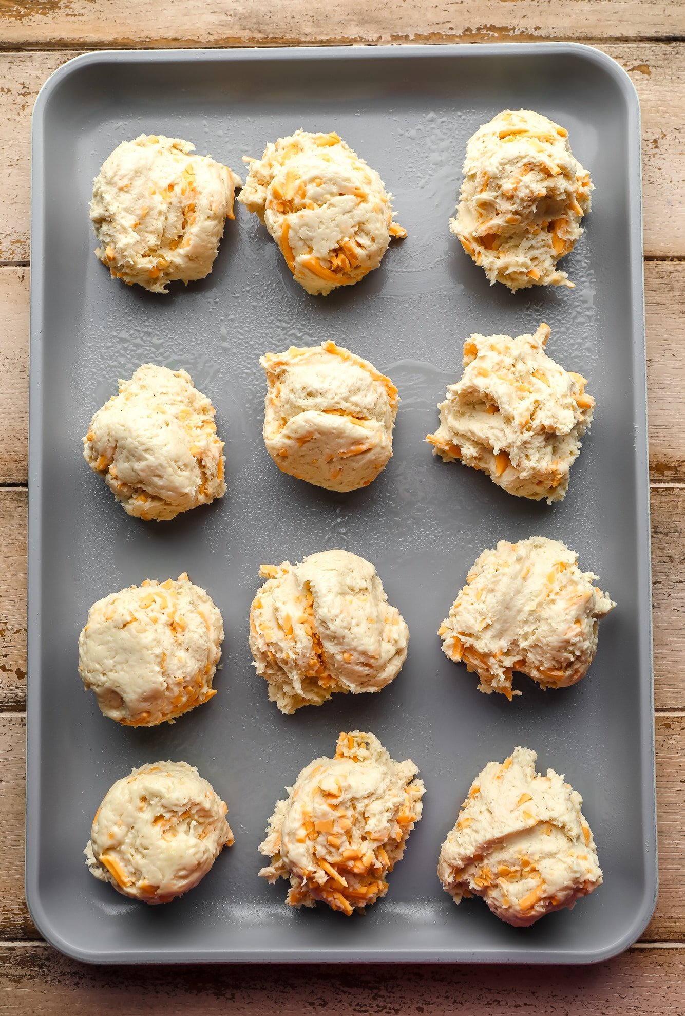 scoops of raw vegan cheddar bay biscuit dough on a metal baking sheet.