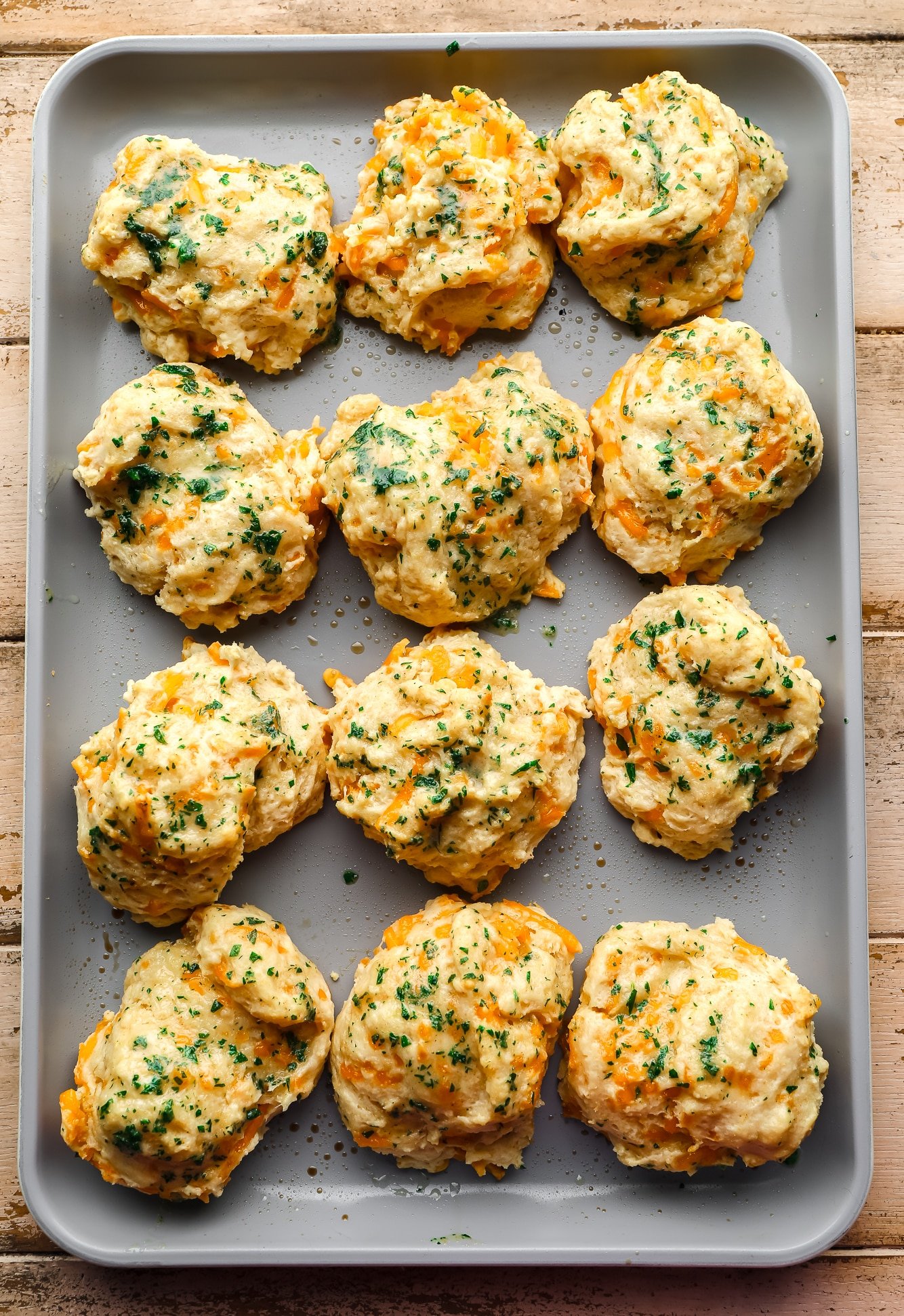 baked vegan cheddar bay biscuits topped with parsley on a metal baking sheet.
