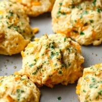 vegan cheddar bay biscuits topped with parsley on a metal baking sheet.