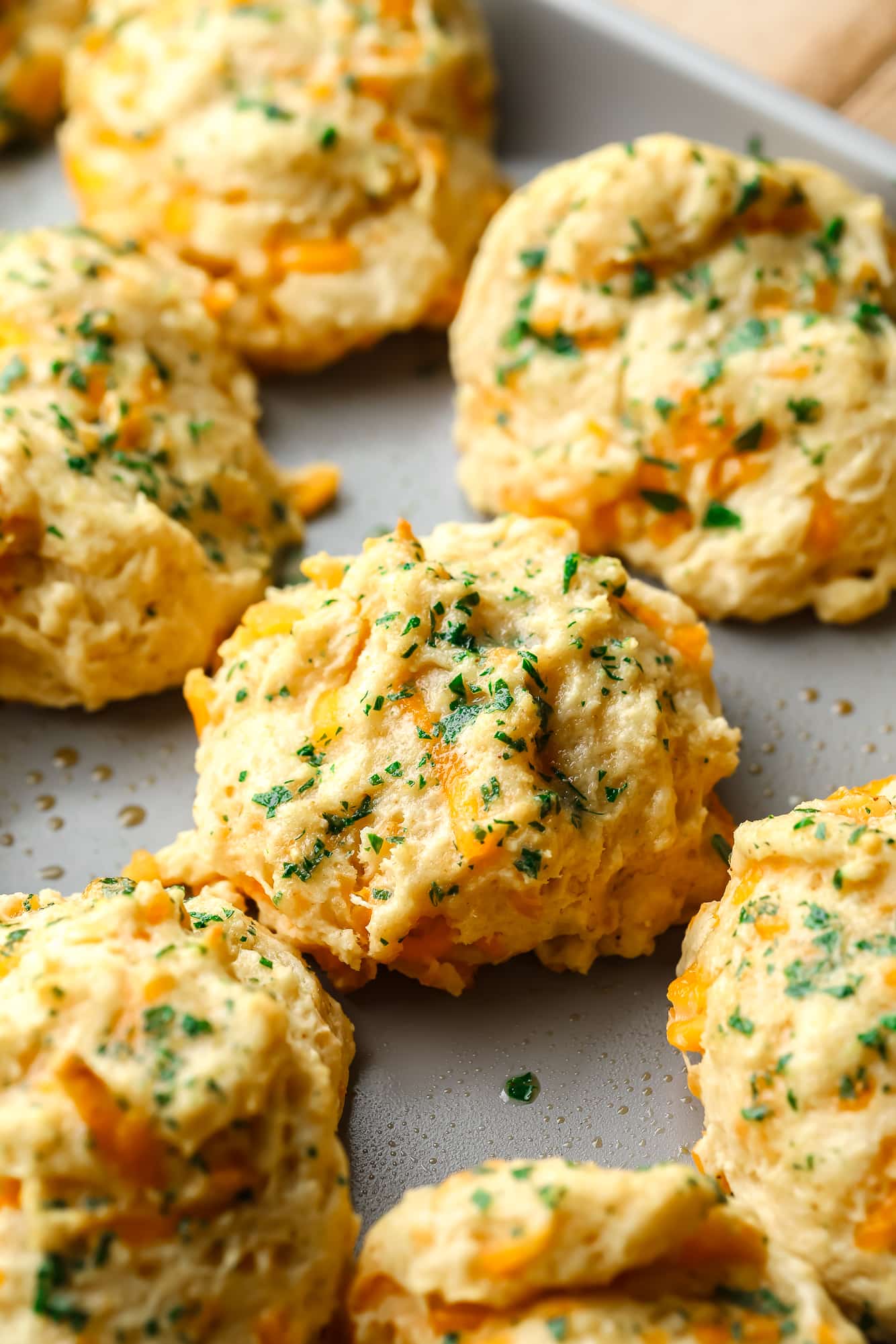 vegan cheddar bay biscuits topped with parsley on a metal baking sheet.