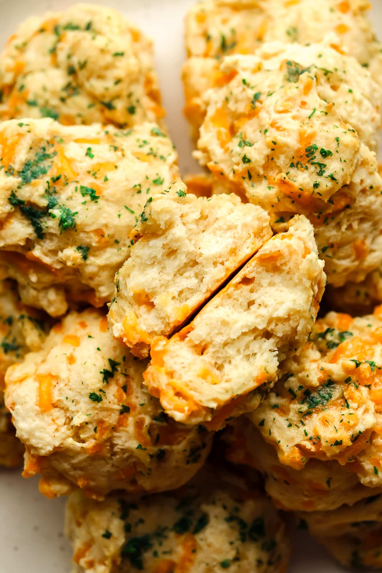 a vegan cheddar bay biscuit torn in half on top of a pile of biscuits.