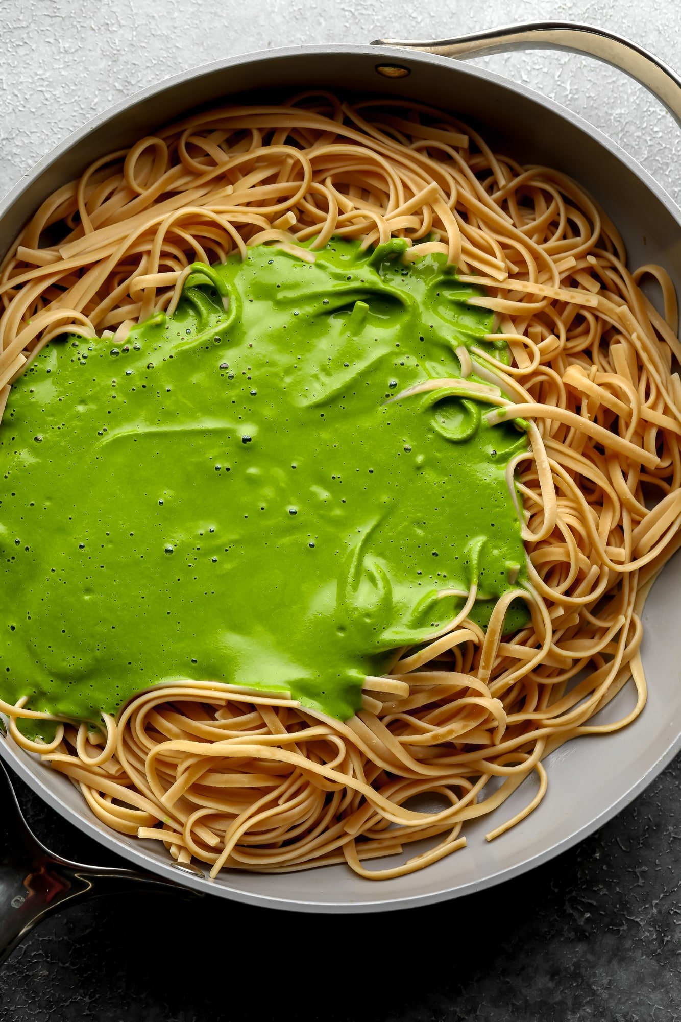 a smooth green sauce on top of cooked pasta noodles in a large grey pot.