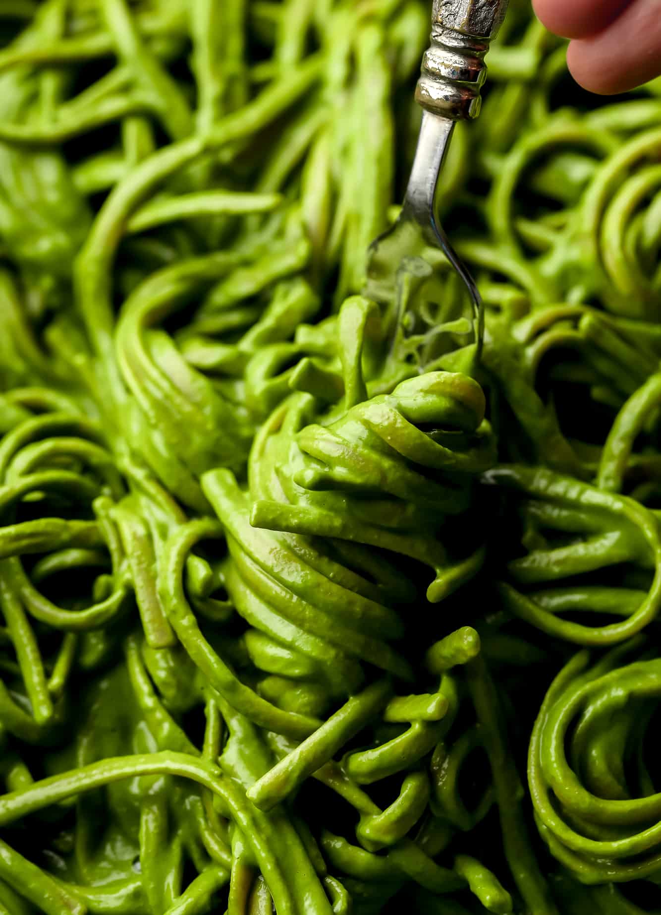 using a fork to twirl a bite of green pasta.