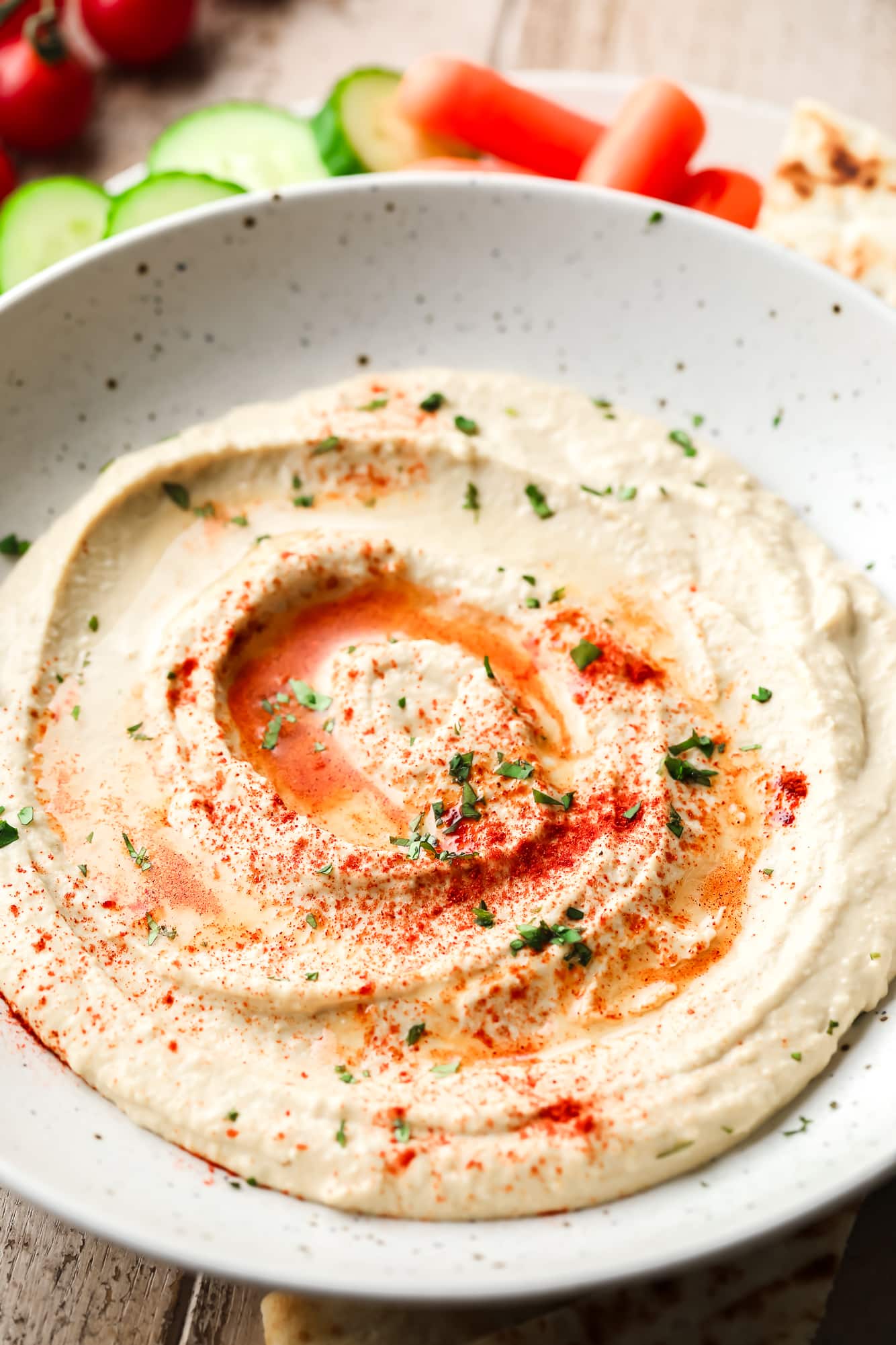 creamy hummus topped with paprika, herbs, and oil in a white bowl.