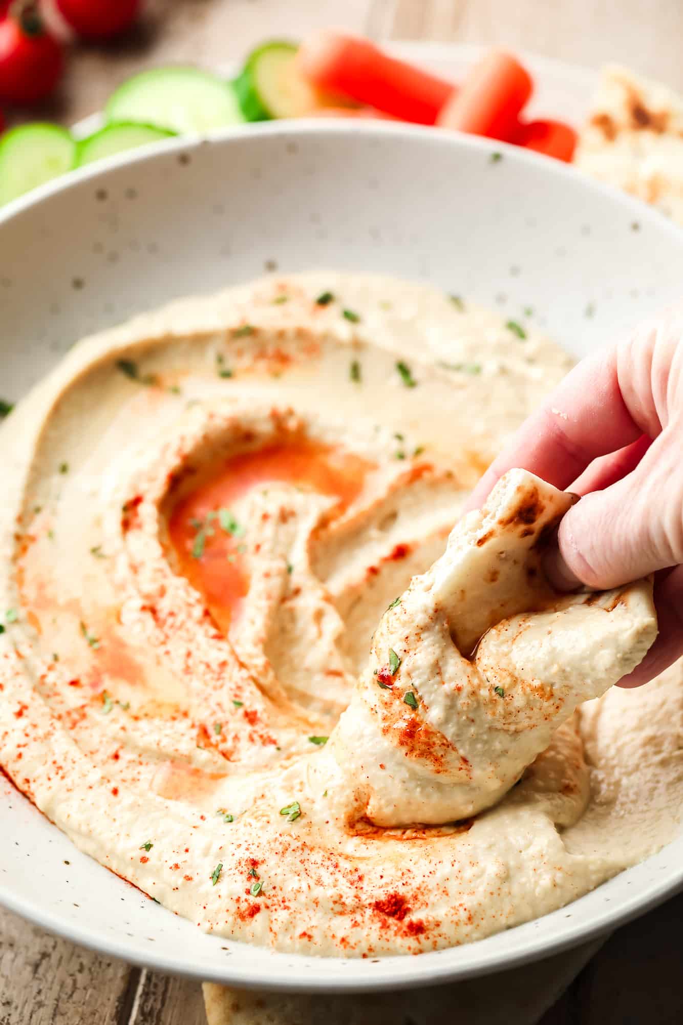 a hand dipping pita bread in a bowl of hummus.