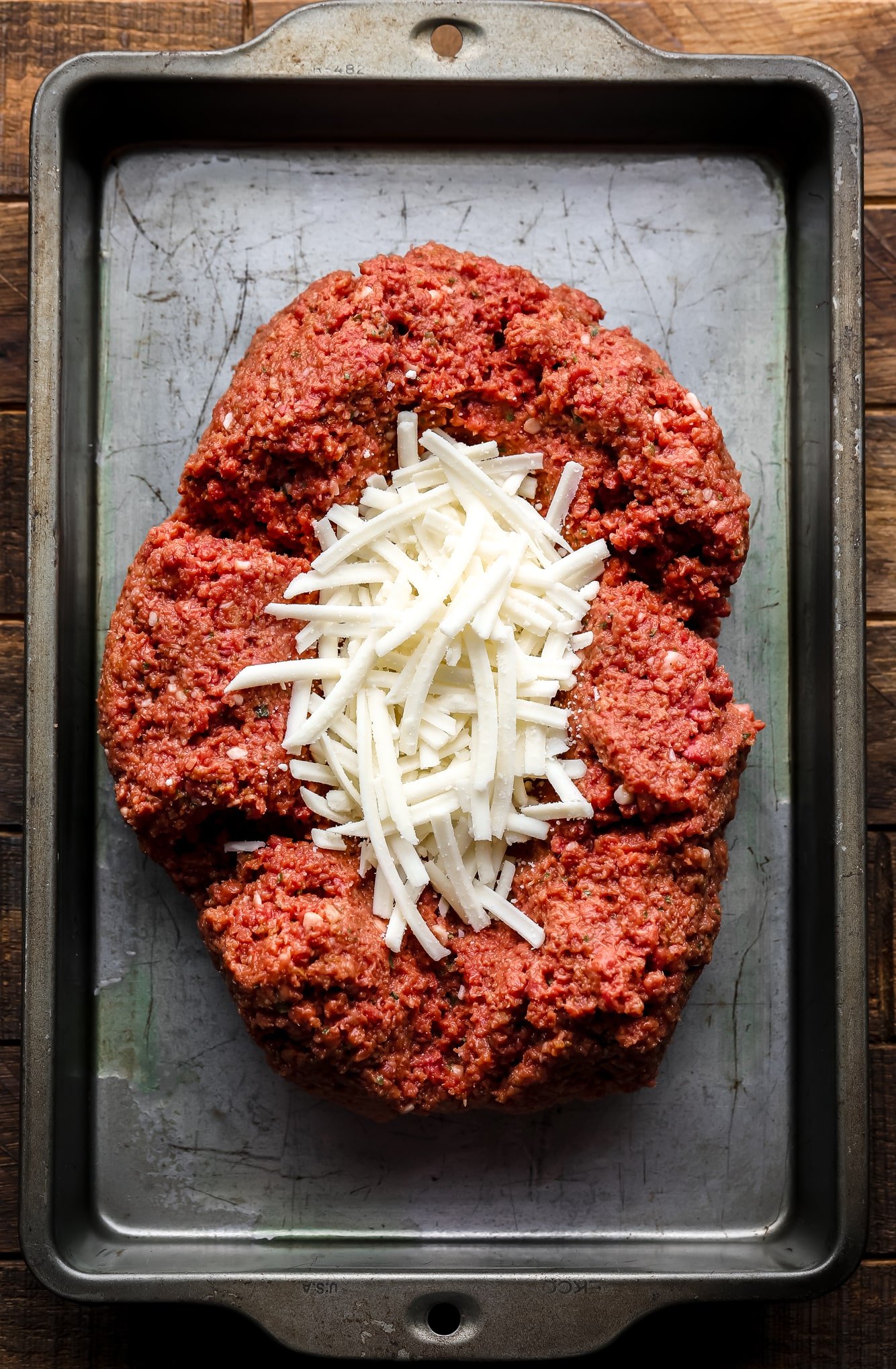 a vegan meatloaf mixture on a sheet pan with shredded vegan mozzarella in the middle.