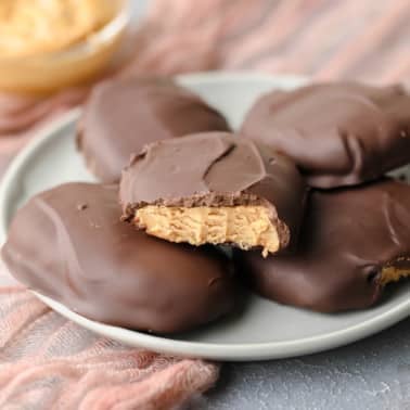 square image of 5 peanut butter chocolate eggs, one a bite taken out of, on a grey plate with pink towel