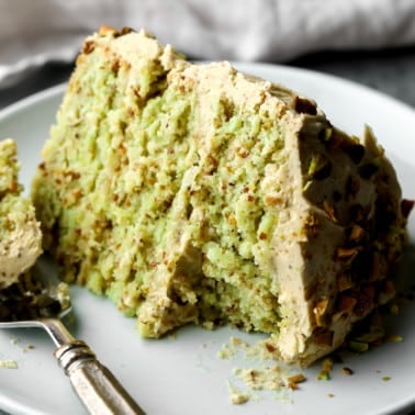 close up on a slice of vegan pistachio cake on a white plate with a bite missing.