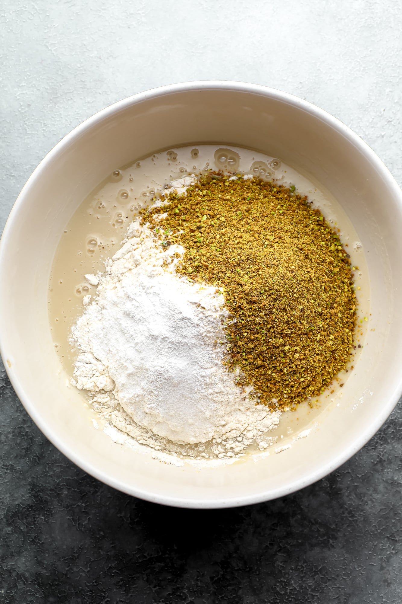 wet and dry ingredients for vegan pistachio cake in a large white bowl.