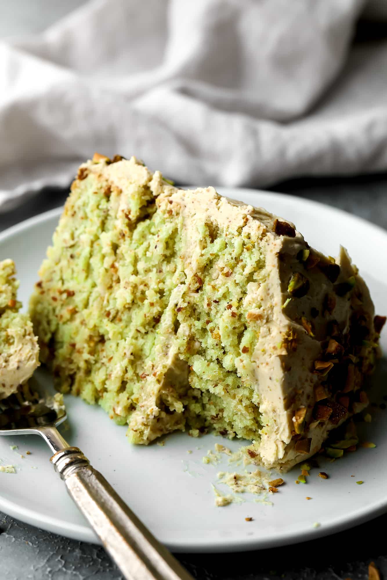 close up on a slice of vegan pistachio cake on a white plate with a bite missing.