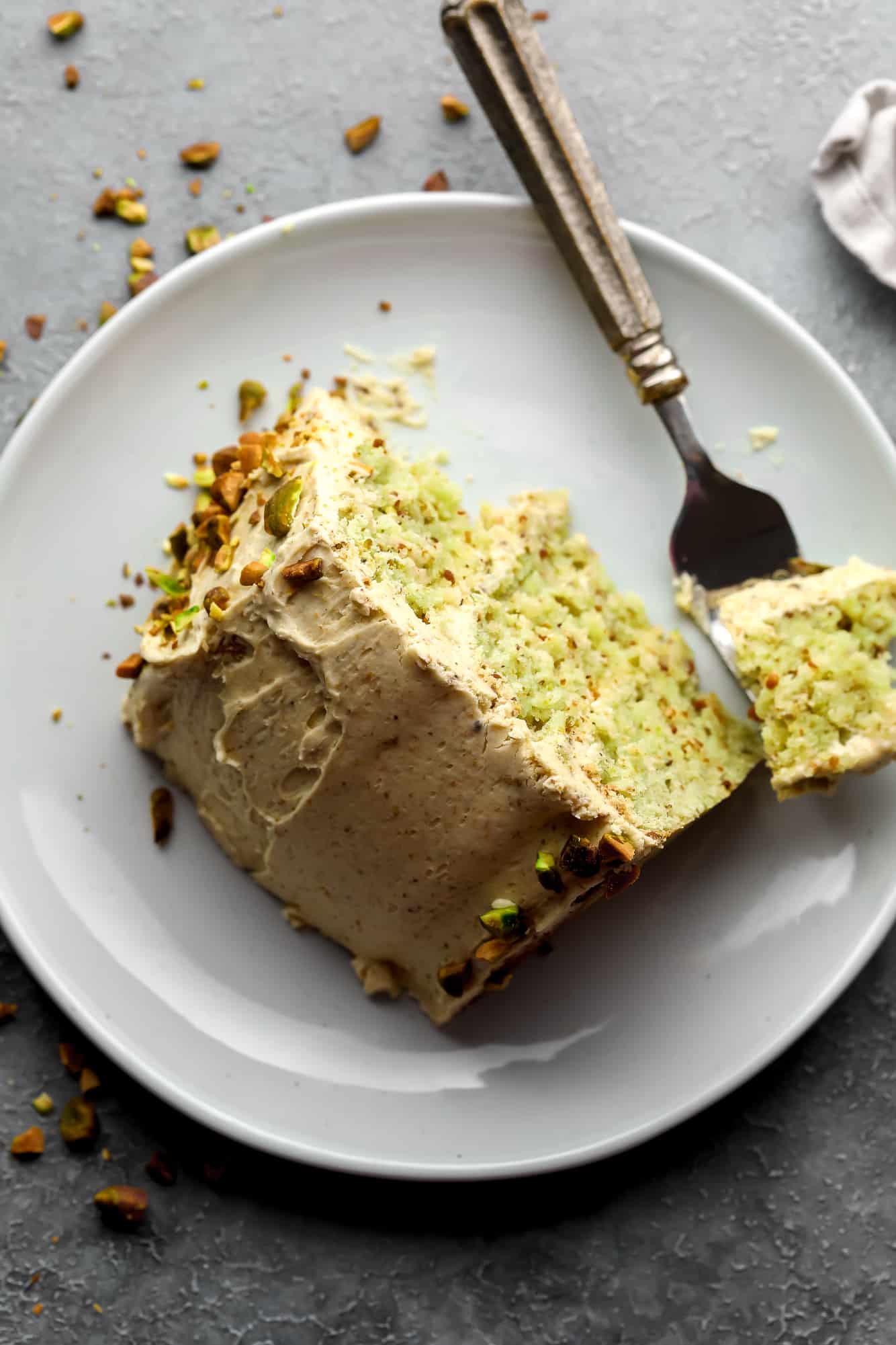a slice of vegan pistachio cake on a white plate with a bite missing.